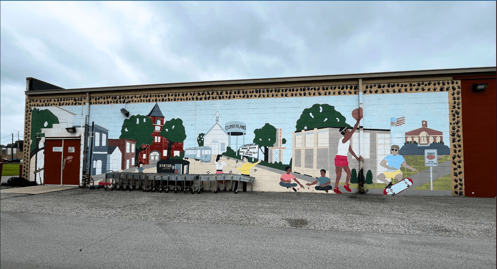 A large community mural painted on the exterior brick wall of a building in Cumberland, Indiana. The mural depicts scenes from local history and everyday life, including a streetcar labeled 
